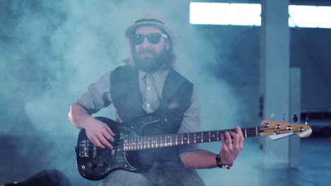 bearded musician playing bass guitar in smoky indoor venue