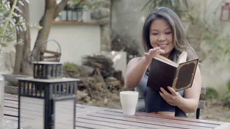 vista frontal de una mujer sentada en el patio trasero y leyendo un libro