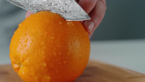 person slicing orange in half on chopping board