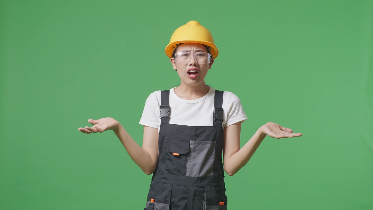 Wondering Asian Woman Worker Wearing Goggles And Safety Helmet Saying Why And Standing Doubtfully In The Green Screen Background Studio