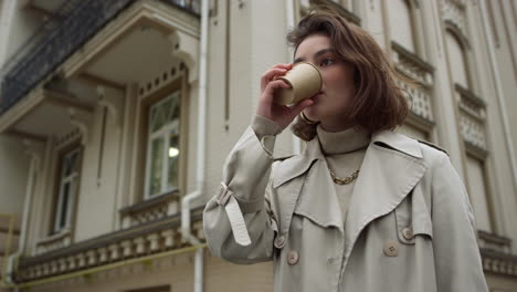 young woman drinking coffee to go on street. girl enjoying hot latte outdoor.