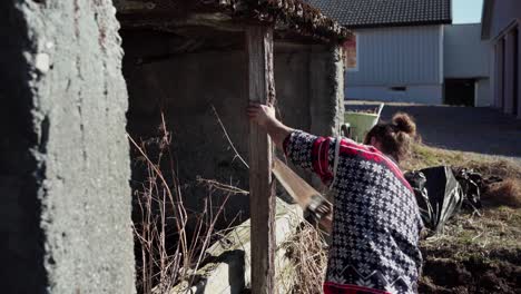 el hombre está usando una sierra para cortar a través del viejo poste de apoyo ubicado en la granja en indre fosen, condado de trondelag, noruega - toma estática
