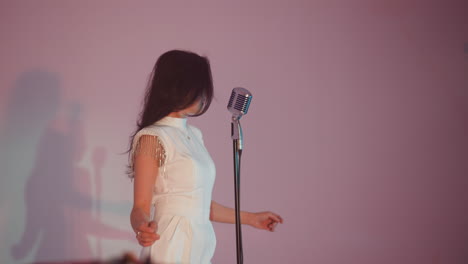 a female singer in a white dress performs in front of a white background, flicking her hair left and right