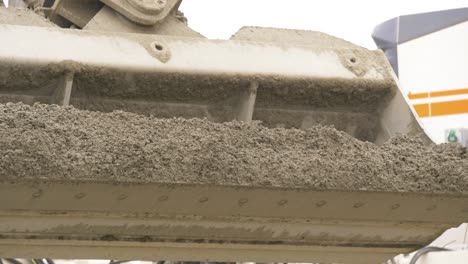 Excavator-bucket-unloads-fresh-concrete-fron-truck-onto-first-layer-of-concrete-road-surface