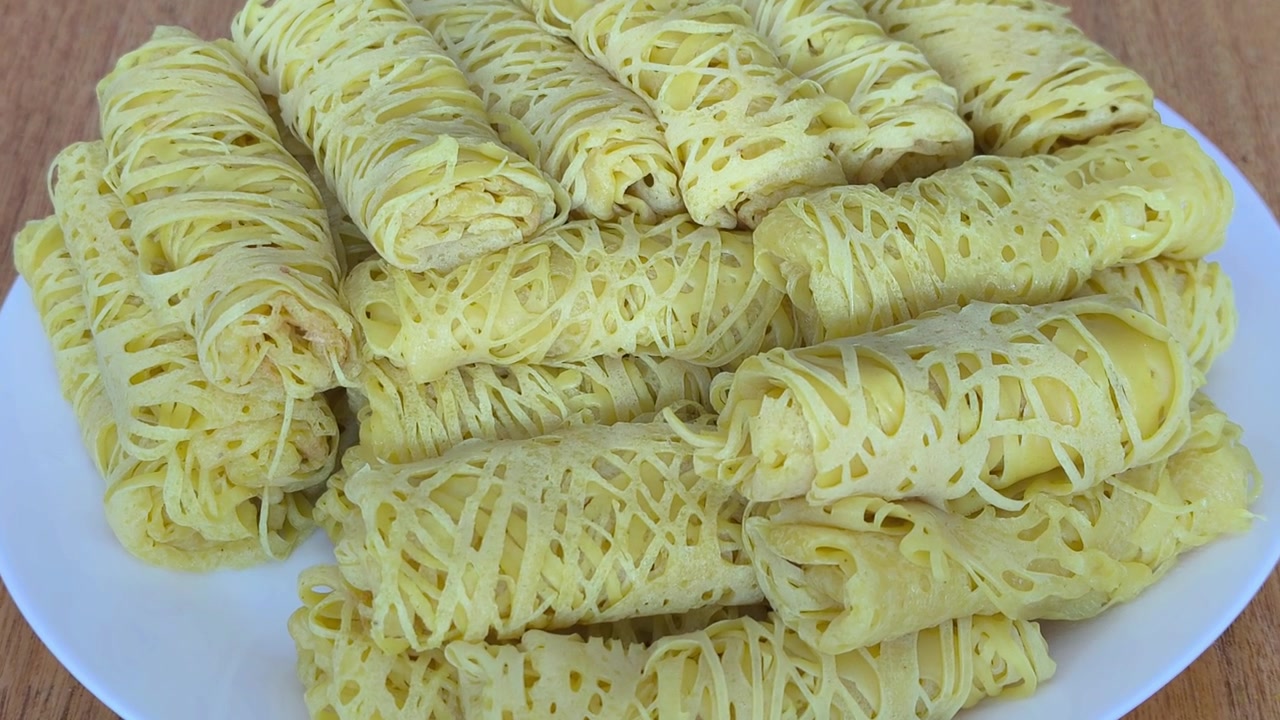 Diverse crepes gialle arrotolate a pizzo sono disposte su un piatto bianco pulito. Questo tradizionale snack malese è conosciuto come roti jala e servito con curry.