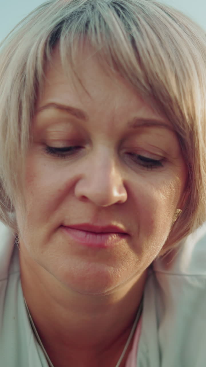 primer plano íntimo de una mujer tranquila y reflexiva con cabello gris, ojos suavemente cerrados, tendida en un vasto campo abierto, el fondo suavemente borroso, creando una atmósfera tranquila y meditativa