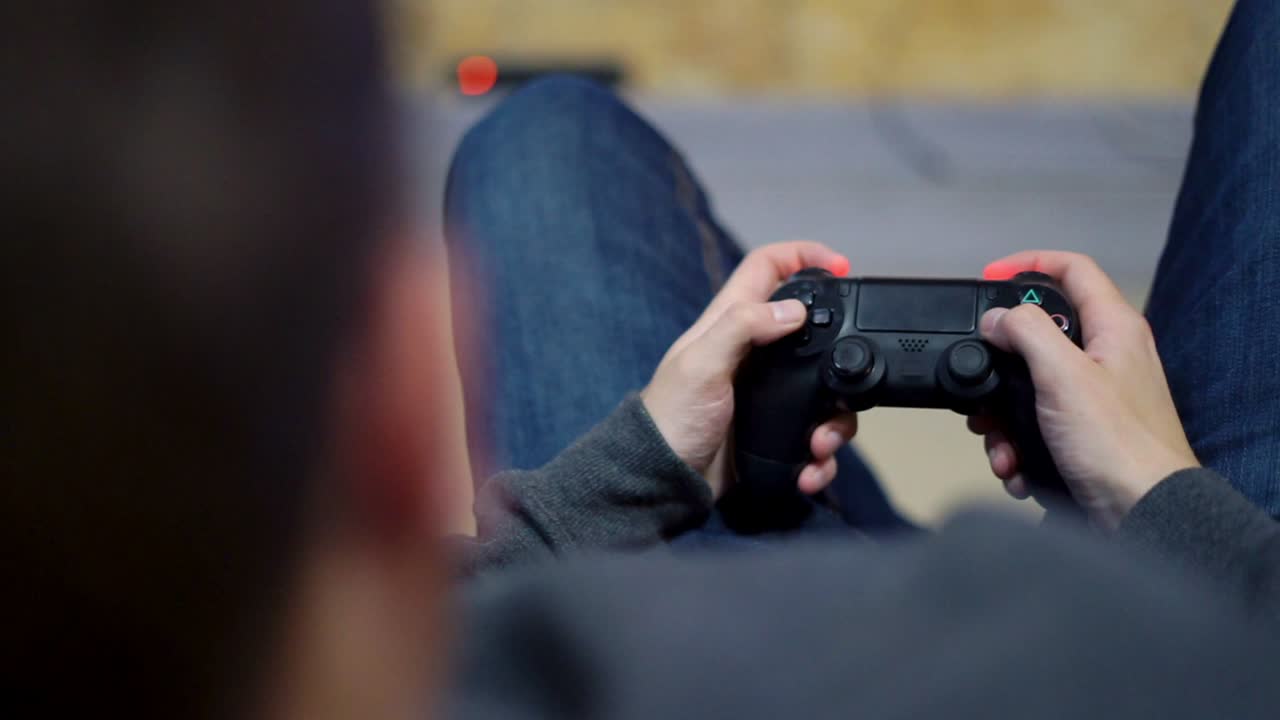 Close Up view of man's hands playing video game at home. Shooting and controlling using the game controller. Wireless game