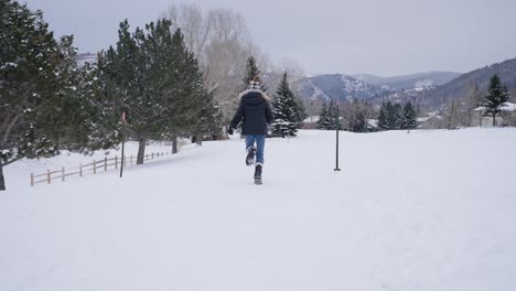 Back-View-of-Young-Teenager-Running-on-Snow-in-Mountain-Landscape-on-Cold-Winter-Day,-Slow-Motion