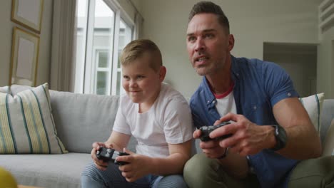 happy caucasian father with son sitting in living room and playing video games