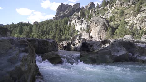 Slow-motion-shot-of-rocky-creek-flowing-downwards-the-river-in-summer-with-beautiful-landscape-in-backdrop