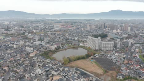 Aerial-view-of-a-populated-city,-with-mist-fog-covered-mountains-on-the-horizon,-Kusatsu,-Japan