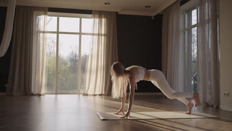 A-young-woman-in-a-white-suit-in-a-gym-trains-yoga-in-the-sun-in-slow-motion