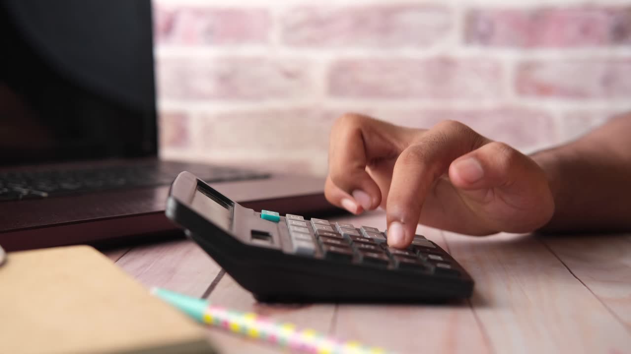 persona usando una calculadora en un escritorio con una computadora portátil