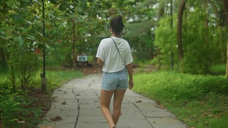 Athletic-fit-brown-skinned-tan-woman-walks-down-tropical-forest-concrete-path,-rear-view