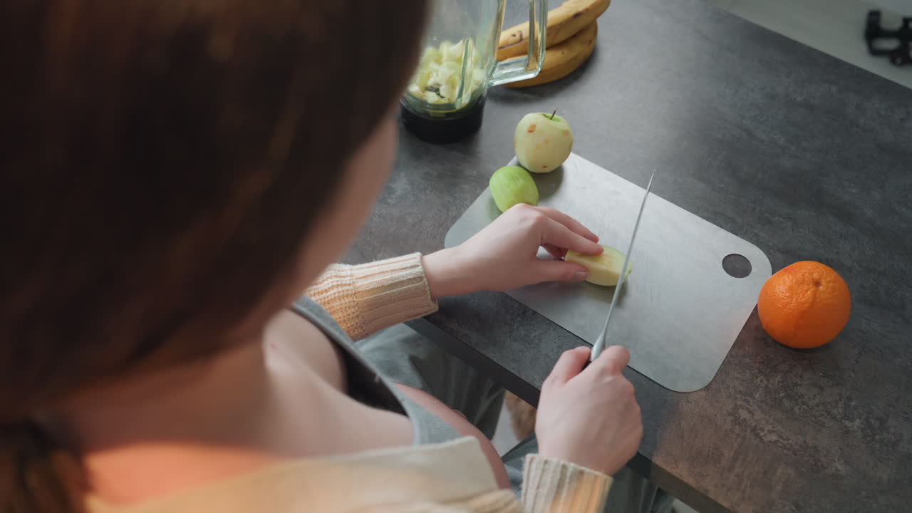 Madre in attesa che taglia una pera vicino a un'arancia, scena di preparazione del pasto prenatale con un delicato uso del coltello, piano di lavoro di casa, attenzione al movimento della mano e al porzionamento, luce diurna intensa, idea di spuntino nutriente per la gravidanza.