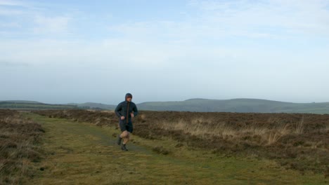 male fitness athlete runner running training in shorts and coat in cold conditions over moorland countryside exmoor uk 4k