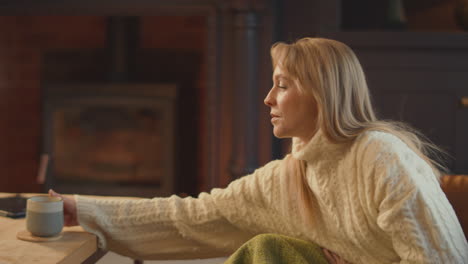 woman at home in lounge with cosy fire with hot drink