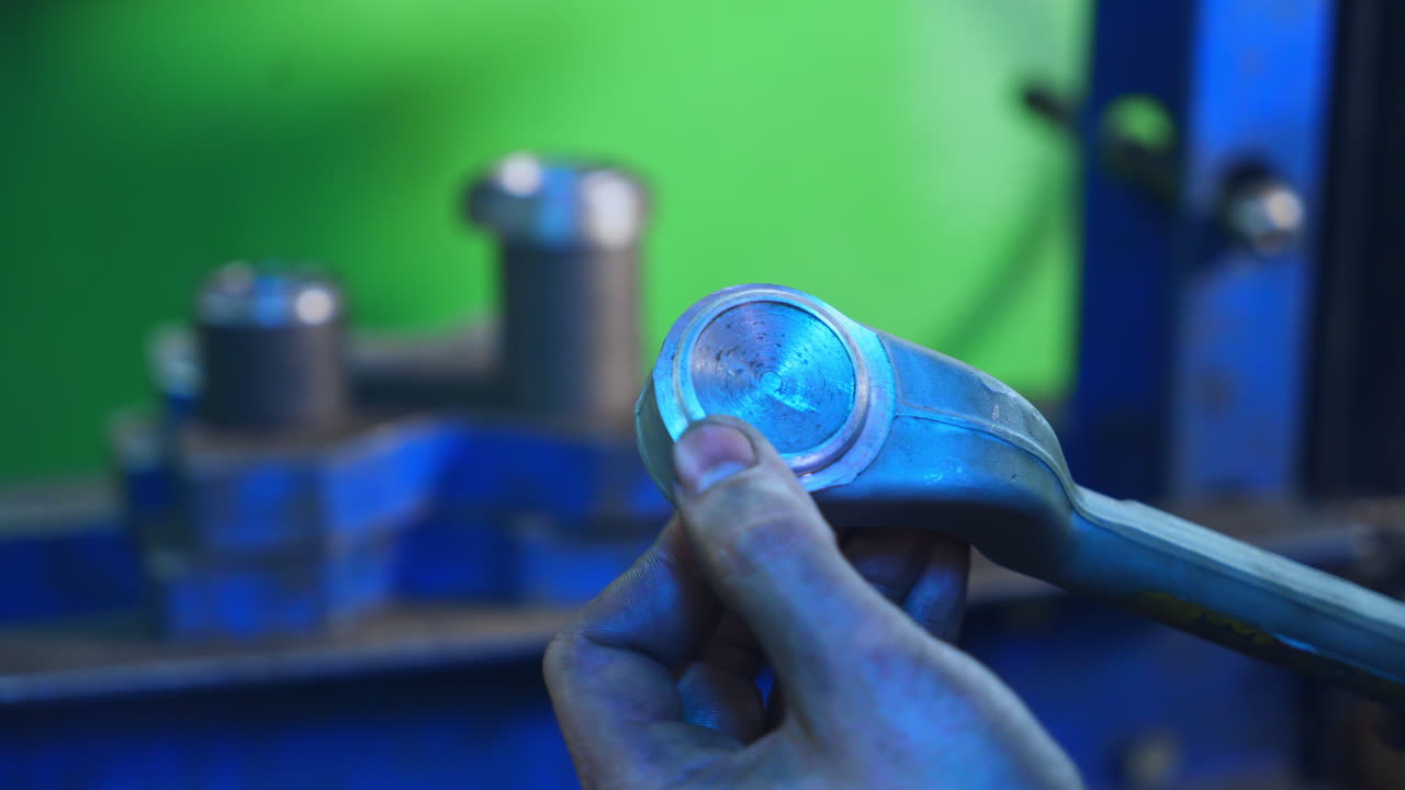 Turner is taking a metal detail and checking it with his fingers. Metal tools and machines at the background in blur.
