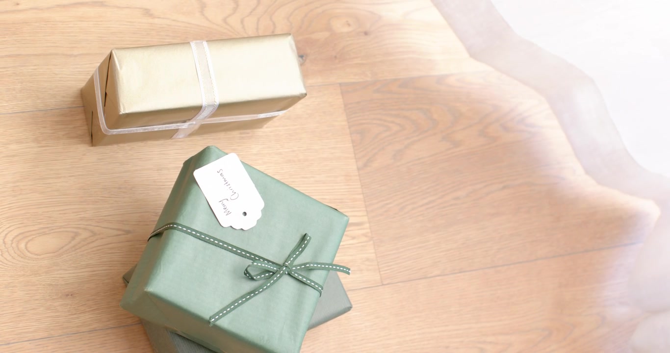White cloth is being pulled right, uncovering green and gold gifts on wooden surface for reveal