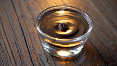 a single coffee bean floating in a glass on a wooden table
