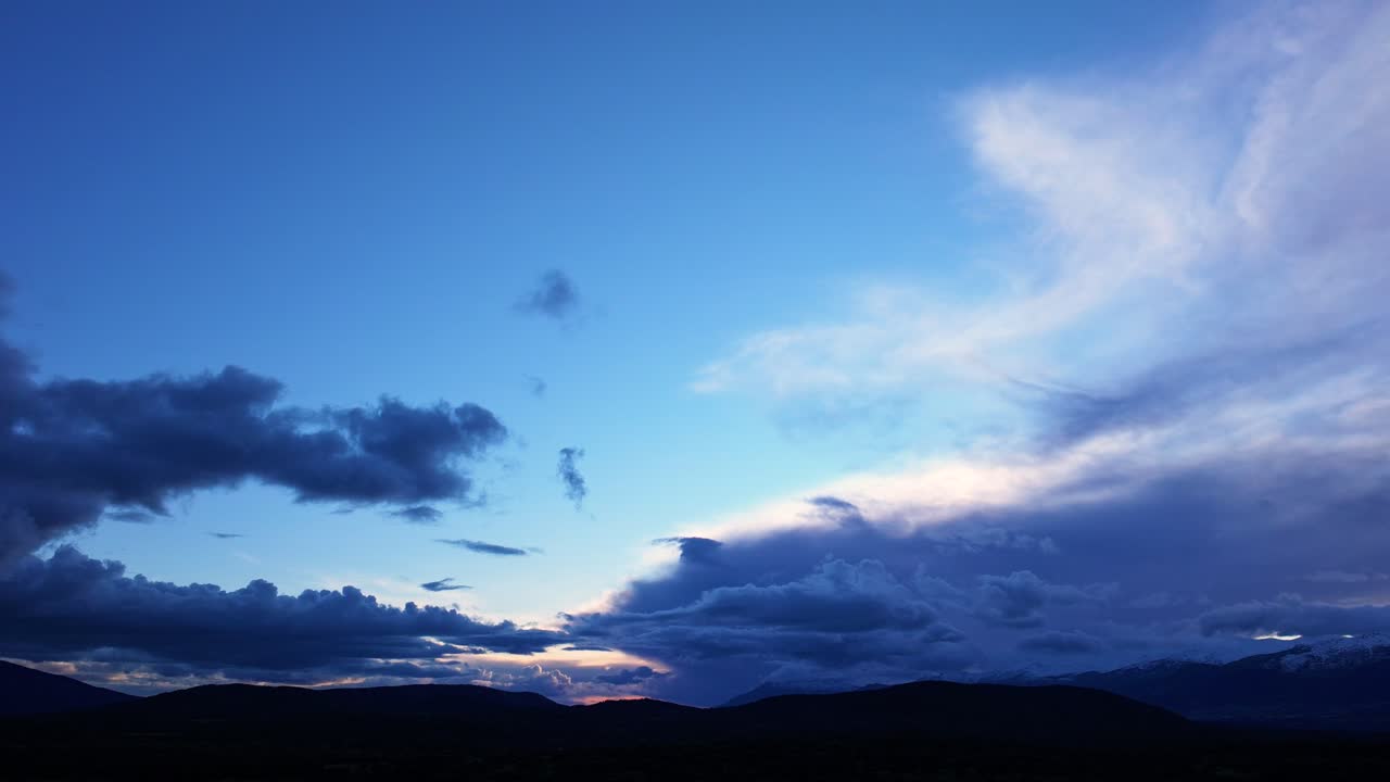 vuelo de avión no tripulado en una puesta de sol en el valle de tietar con un cielo azul y nubes bajas corriendo a velocidad a través del hiperlapso sobre algunas montañas oscurecidas por la luz provincia de ávila, españa