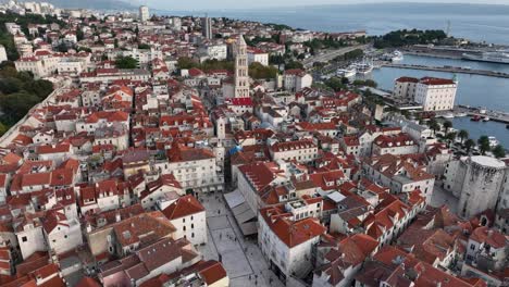 coastal city with red rooftops and harbor in the distance, aerial view