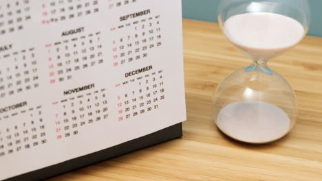 primer plano de un calendario y reloj de arena en la mesa de madera