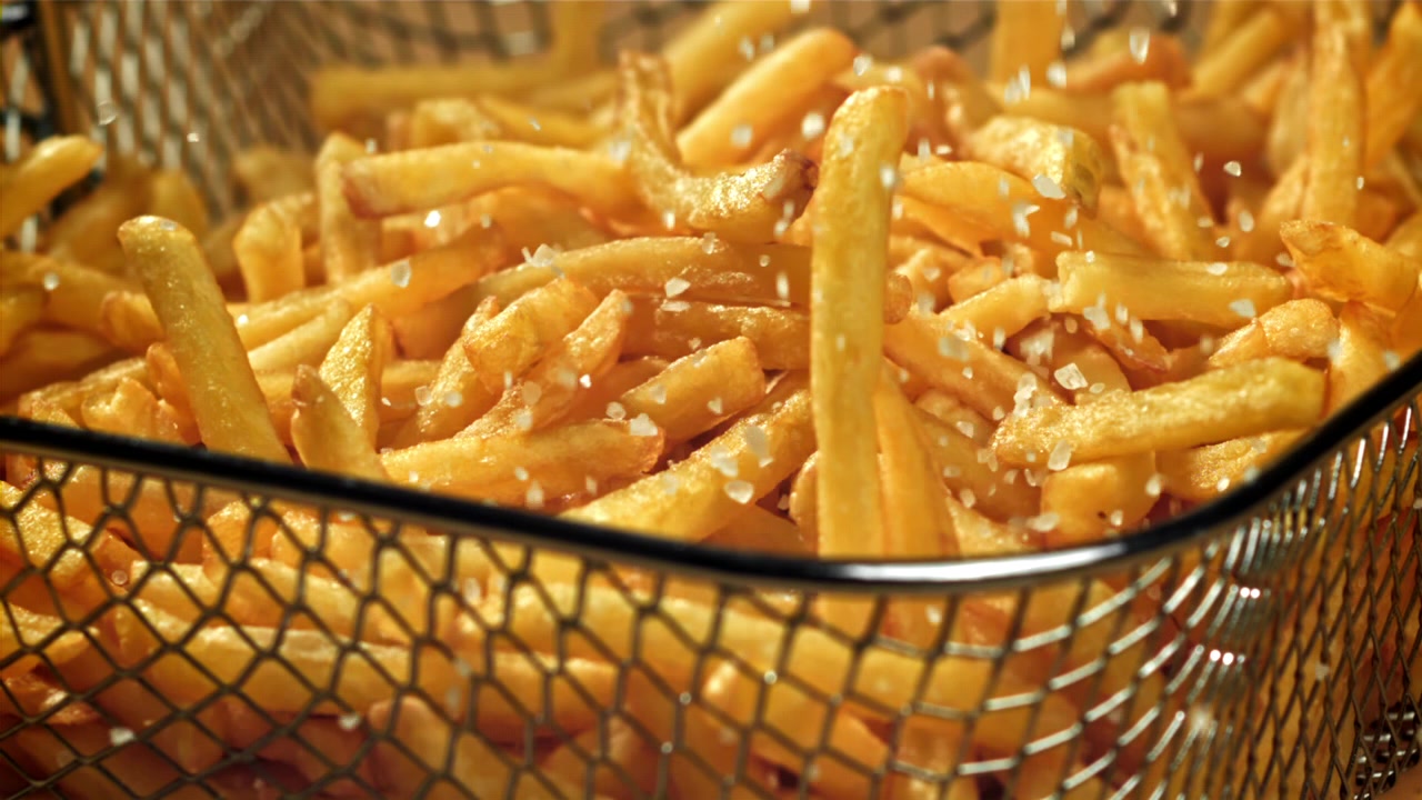 Primer plano en cámara lenta de sal cayendo sobre papas fritas doradas