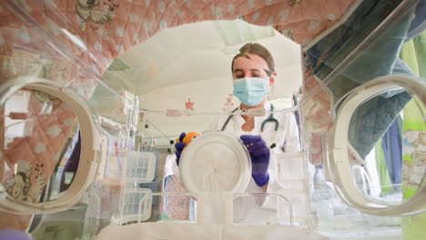 doctor examining baby in incubator with toy