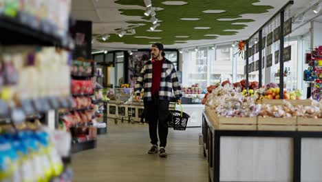 Side-view-of-a-thoughtful-man-in-a-black-cap-examining-the-supermarket-shelves-and-choosing-the-goods-he-needs-during-his-shopping