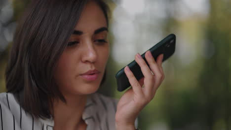 multitasking hispanic businesswoman using voice recognition function on a smartphone standing near desk and typing on the laptop. arabian female entrepreneur sending a vocal message