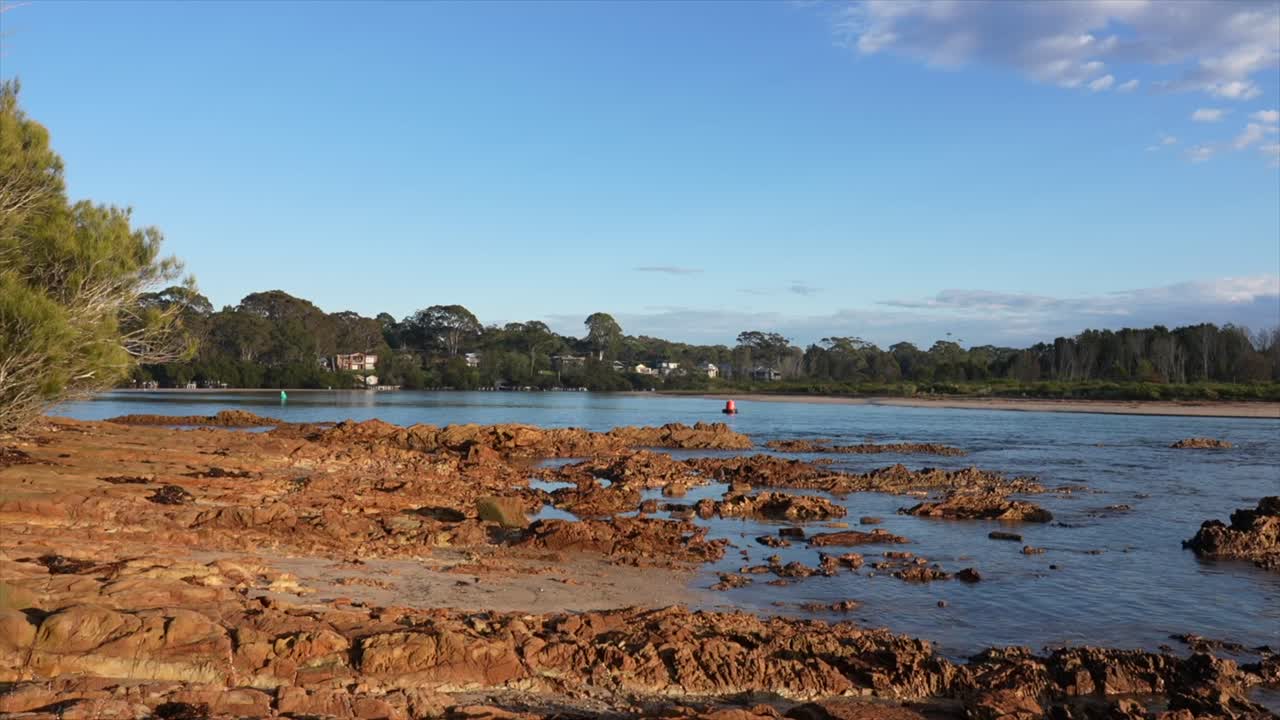 Costa rocciosa esposta e acqua calma dell'estuario a Mossy Point, sulla costa meridionale del Nuovo Galles del Sud, immortalati sotto la luce limpida del mattino poco dopo l'alba