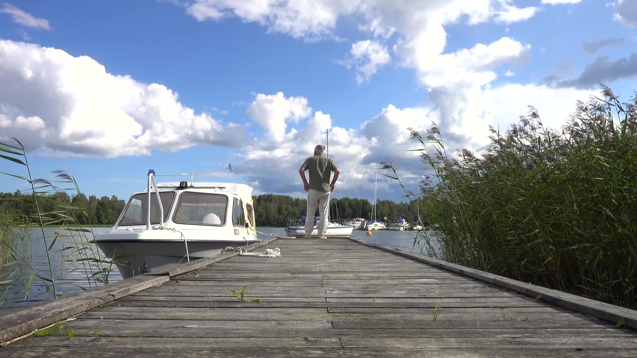 Unidentified man in white linen pants walks along the jetty and stops. Norrtälje, Sweden.