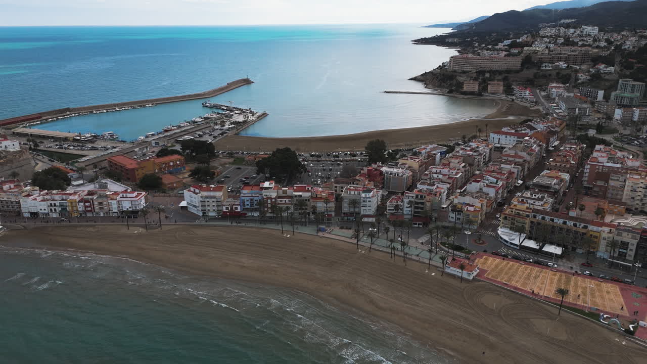 Drone captures beach curve and waterfront of Peniscola under early morning sunlight