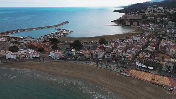 Drone riprende la curva della spiaggia e il lungomare di Peñíscola sotto la luce del sole del primo mattino.
