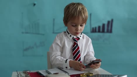 good looking, smart casual dressed child, blond boy with tie, working on tablet, taking notes and talking on the phone, business concept and idea