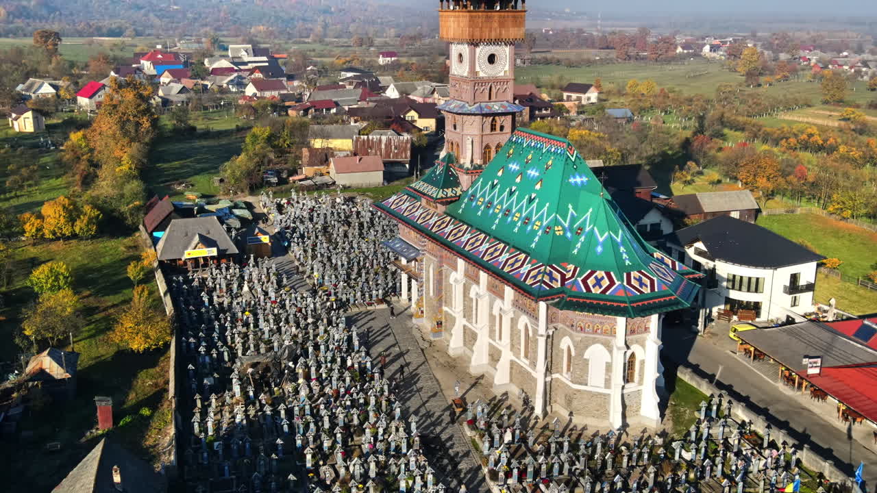Aerial drone view of The Merry Cemetery in Sapanta, Romania. Church and multiple tombstones, visitors, residential buildings, yellowing trees