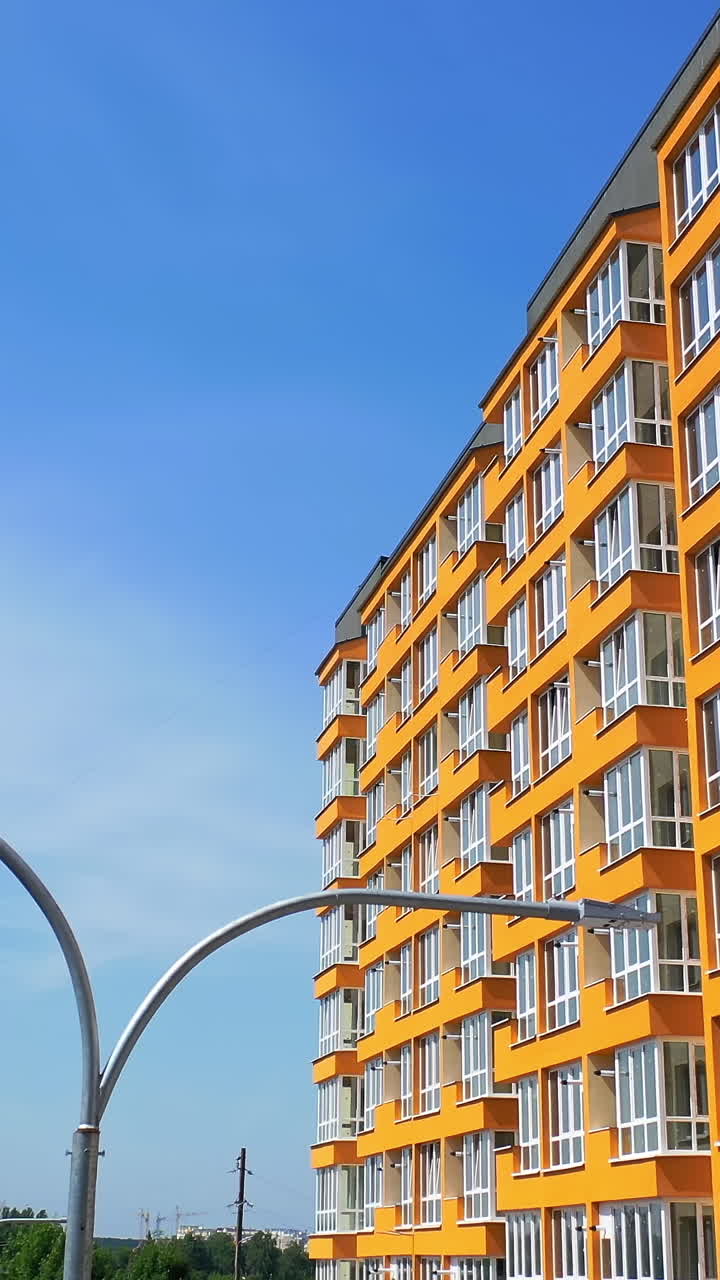 Modern skyscraper of bright color. New multi storey building in the city. Side view of contemporary high-rise against blue sky background. Vertical video