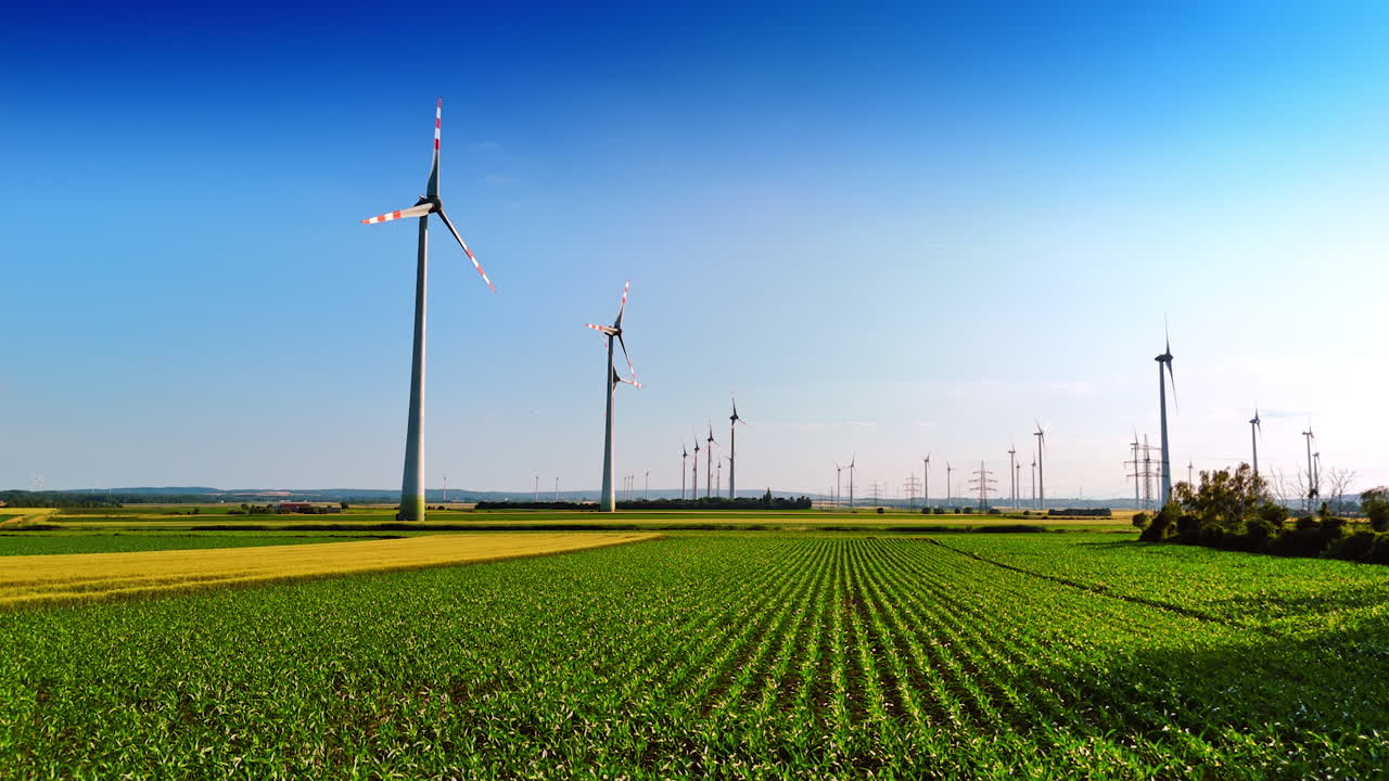 Footage over the green agricultural field. Low angle view at the wind turbines rotating in the plantation.