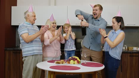 Multigenerational-family-members-with-child-girl-kid-celebrating-birthday-party.-Opening-champagne