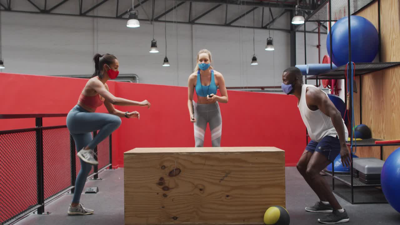 Coach signaling and counting, group doing box jumps in gym, animated mask icons showing for fitness