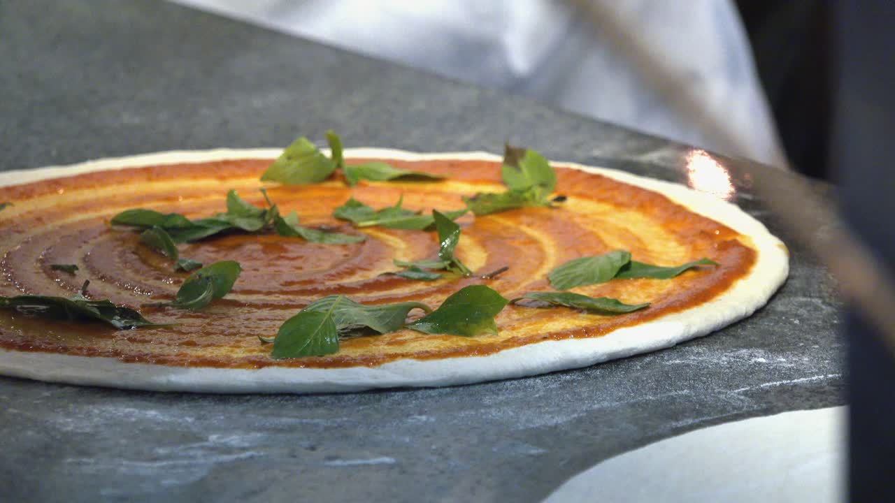 chef preparando pizza con albahaca y queso mozzarella