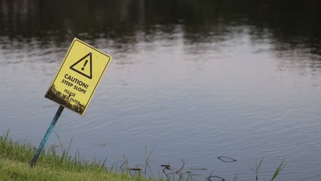 yellow caution sign gently swaying by water.