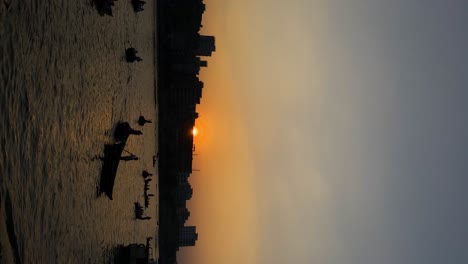 silhouette of local boatmen on buriganga river against orange sunset skies