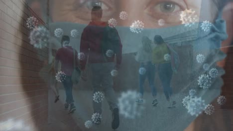 mujer caucásica con una máscara facial y células covid-19 contra los estudiantes que caminan en el corredor de la universidad