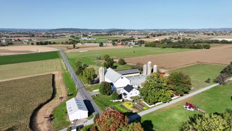 aerial approaching shot of american farm with silo and barn building. sunny autumn day in agricultural landscape of midwest. landing shot.