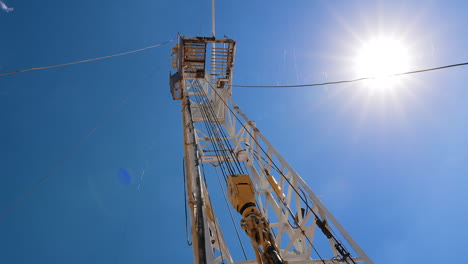 oil rig tower with attached equipment for drilling. low angle view on the support at the backdrop of blue sky and bright sun.