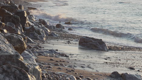 morning sun is reflected on rocky sea coast as waves wash on shore calmly