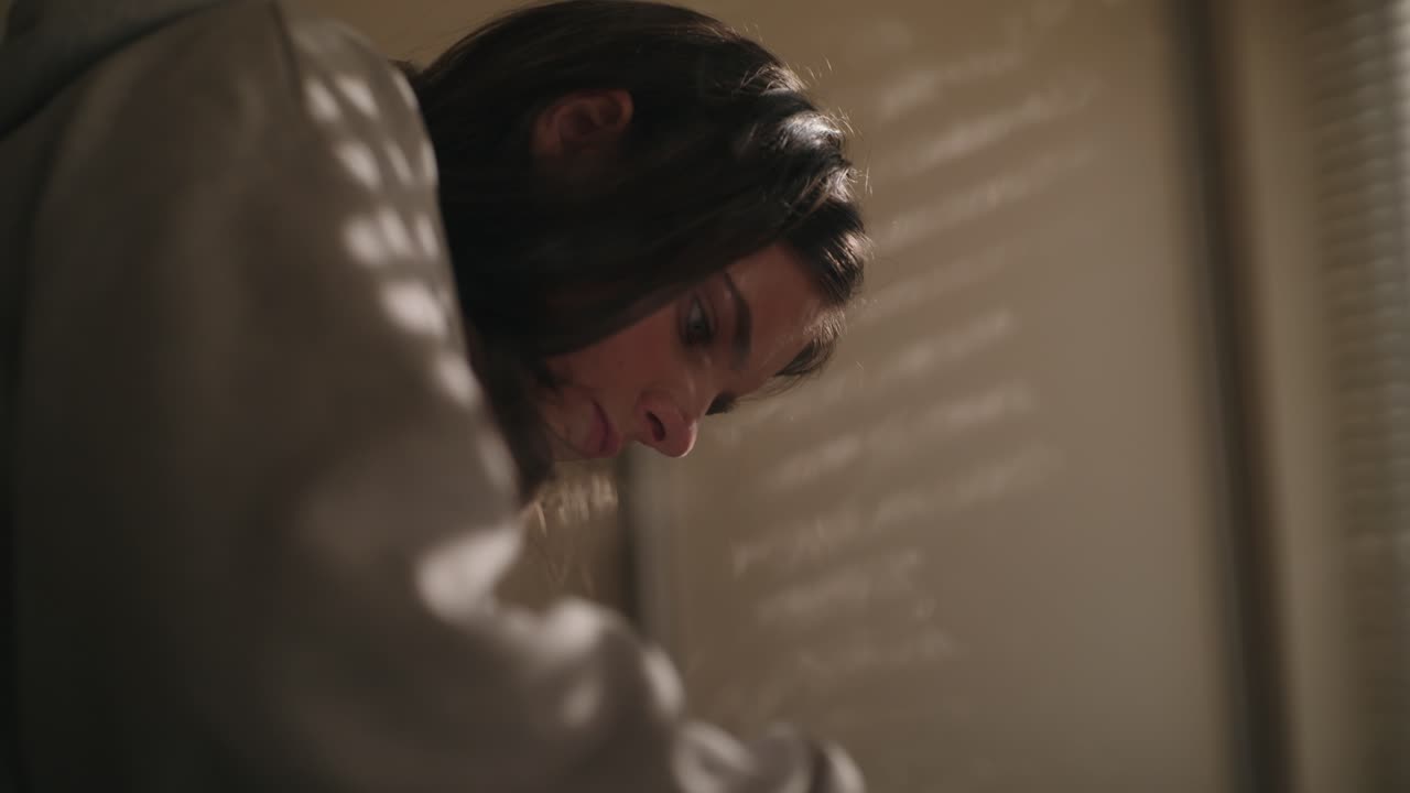 Intimate close-up of a woman concentrating during a task in soft window light. Subtle shadow patterns create a moody Irish domestic scene.