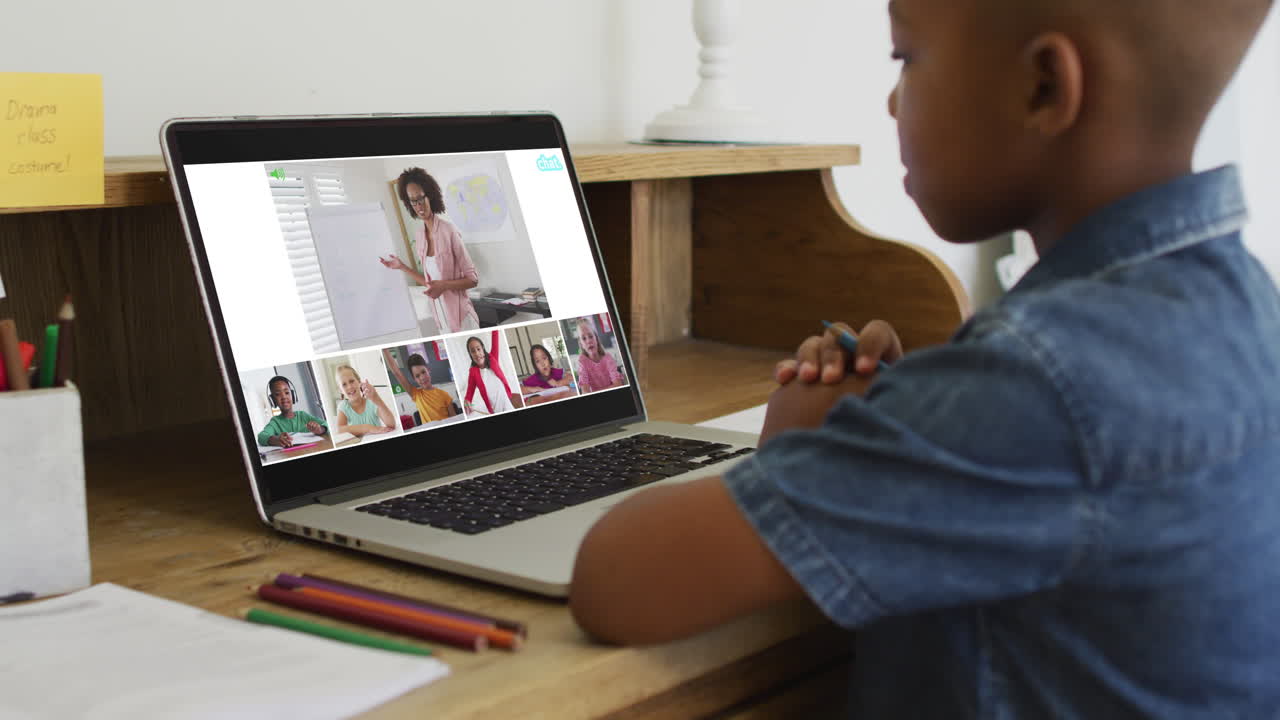 niño afroamericano sosteniendo un lápiz teniendo una videoconferencia en una computadora portátil en casa